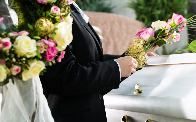 Mourning man and woman on funeral with pink rose standing at casket or coffin