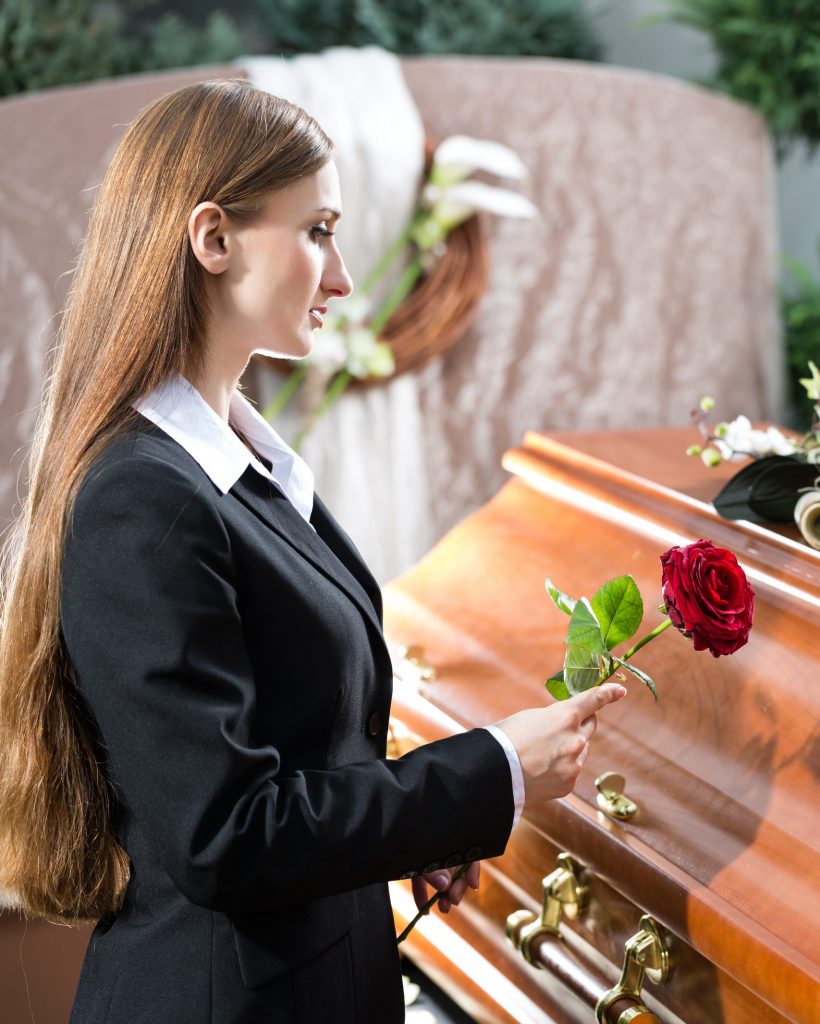 Mourning woman on funeral with red rose standing at casket or coffin